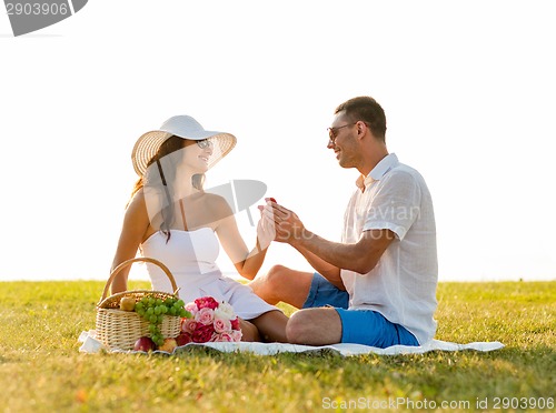 Image of smiling couple with small red gift box on picnic