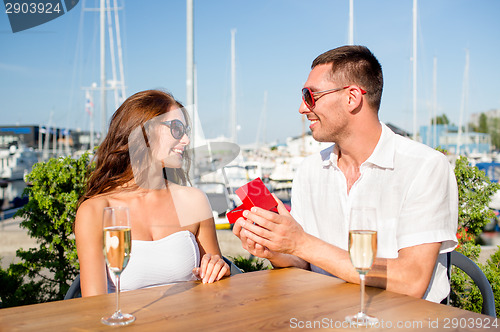 Image of smiling couple with champagne and gift at cafe