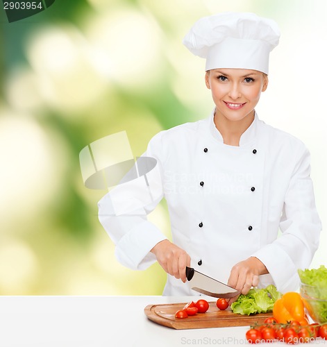 Image of smiling female chef chopping vegetables