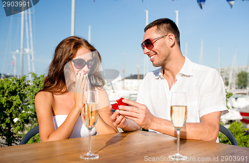 Image of smiling couple with champagne and gift at cafe