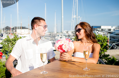 Image of smiling couple with bunch and champagne at cafe