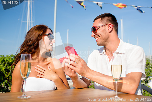 Image of smiling couple with champagne and gift at cafe