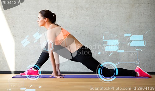 Image of smiling woman stretching leg on mat in gym