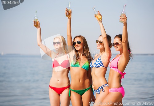 Image of group of smiling young women drinking on beach