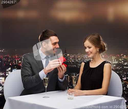 Image of excited young woman looking at boyfriend with box