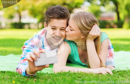 Image of smiling couple making selfie and kissing in park