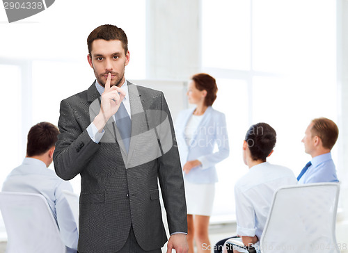 Image of group of smiling businessmen making hush sign