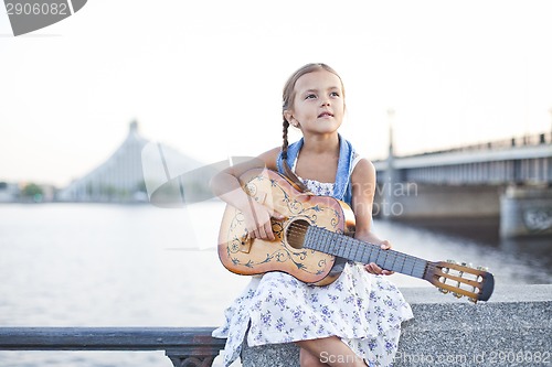 Image of Girl playing guitar on river embankment