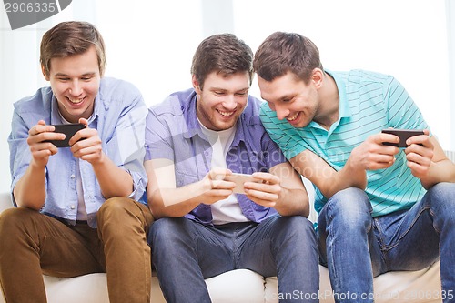 Image of smiling friends with smartphones at home