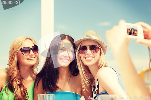 Image of girls taking photo with digital camera in cafe