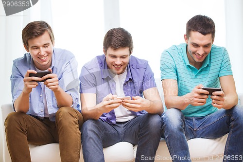 Image of smiling friends with smartphones at home