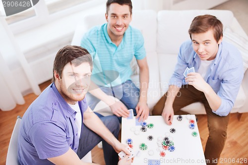 Image of three smiling male friends playing cards at home