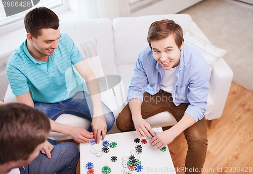 Image of three smiling male friends playing cards at home