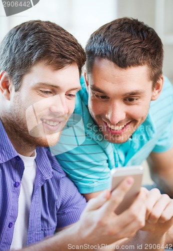 Image of smiling friends with smartphone at home