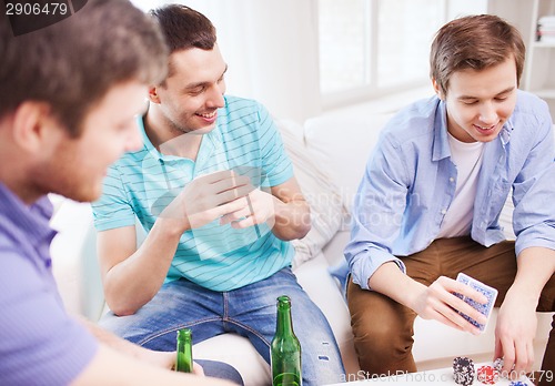 Image of smiling male friends playing cards at home