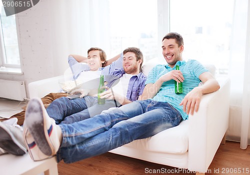 Image of happy male friends with beer watching tv at home