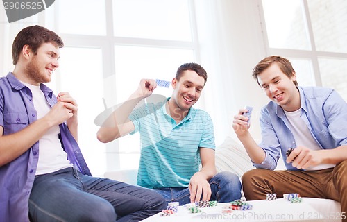 Image of three smiling male friends playing cards at home