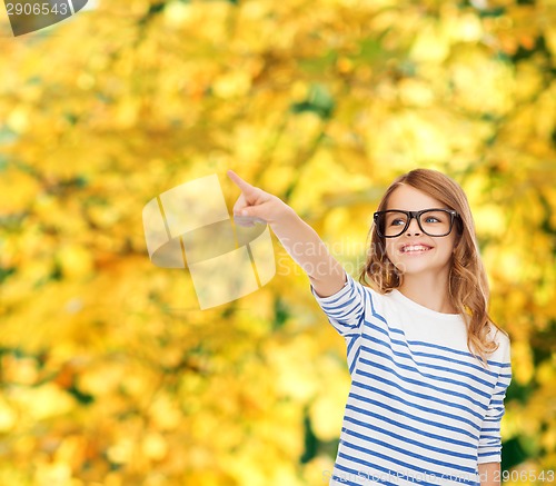 Image of cute little girl in eyeglasses pointing in the air