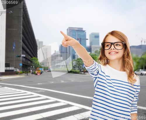 Image of cute little girl in eyeglasses pointing in the air