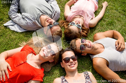 Image of group of smiling friends lying on grass outdoors