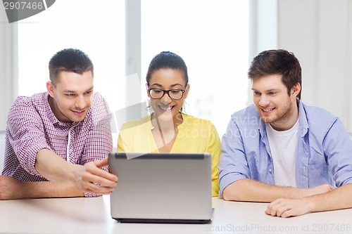 Image of three smiling colleagues with laptop in office