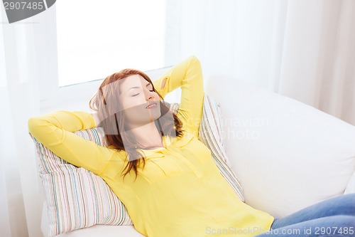 Image of smiling young woman lying on sofa at home