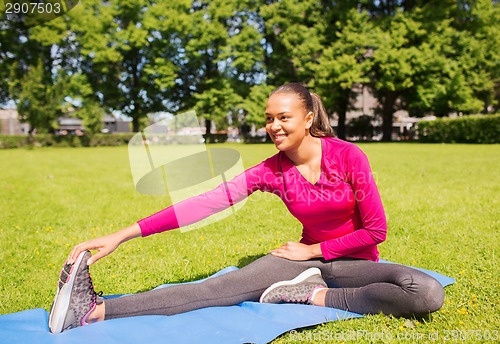 Image of smiling woman stretching leg on mat outdoors