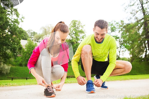 Image of smiling couple tying shoelaces outdoors