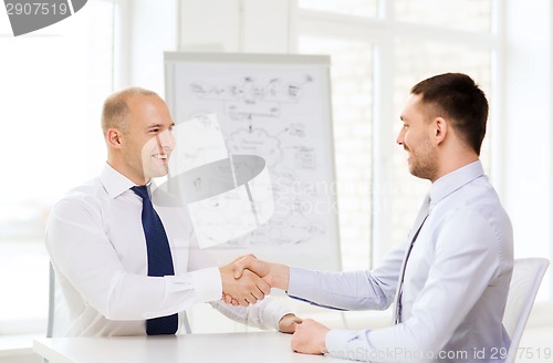 Image of two smiling businessmen shaking hands in office