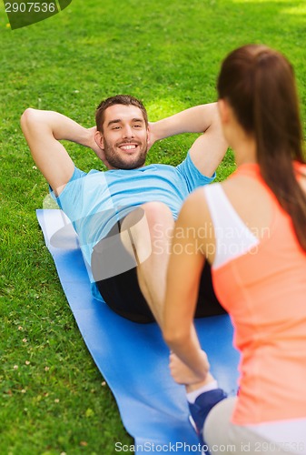 Image of smiling man doing exercises on mat outdoors