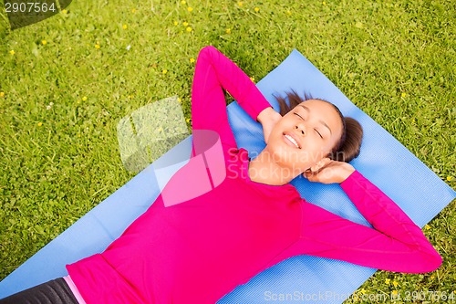 Image of smiling woman doing exercises on mat outdoors