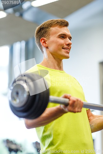 Image of smiling man doing exercise with barbell in gym