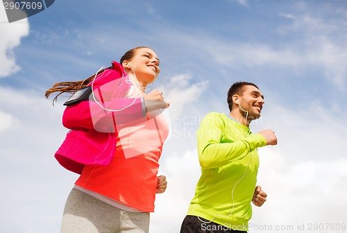 Image of smiling couple with earphones running outdoors