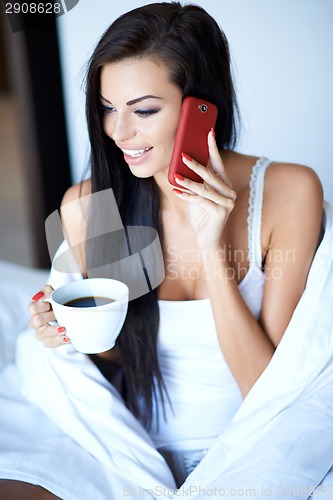 Image of Beautiful woman chatting on a mobile in bed