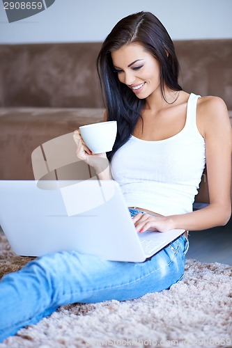 Image of Woman drinking coffee as she types on her laptop