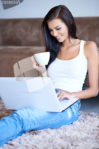 Image of Woman drinking coffee as she types on her laptop