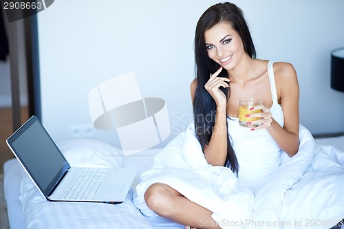 Image of Smiling woman working on her laptop in bed