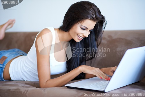 Image of Young woman lying on a sofa using a laptop