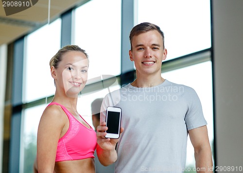 Image of smiling young woman with personal trainer in gym