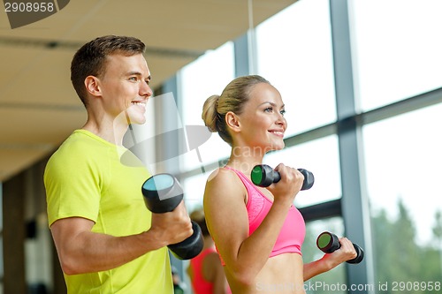 Image of smiling man and woman with dumbbells in gym