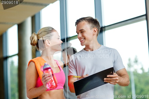 Image of smiling young woman with personal trainer in gym