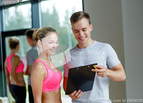 Image of smiling young woman with personal trainer in gym