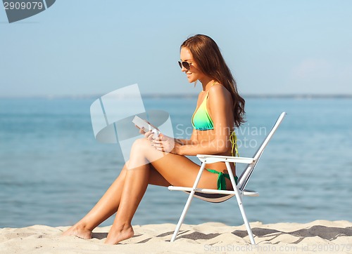 Image of smiling young woman sunbathing in lounge on beach