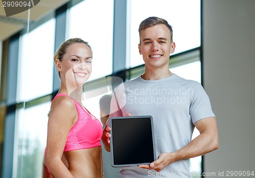 Image of smiling young woman with personal trainer in gym