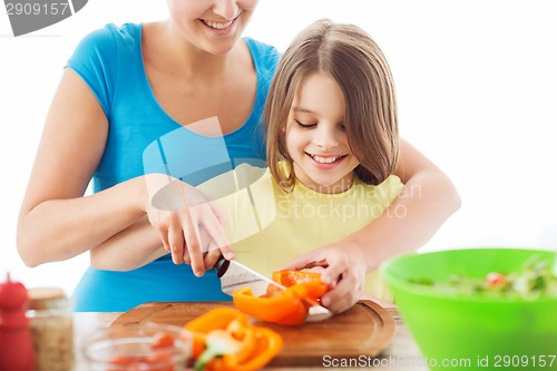 Image of smiling little girl with mother chopping pepper