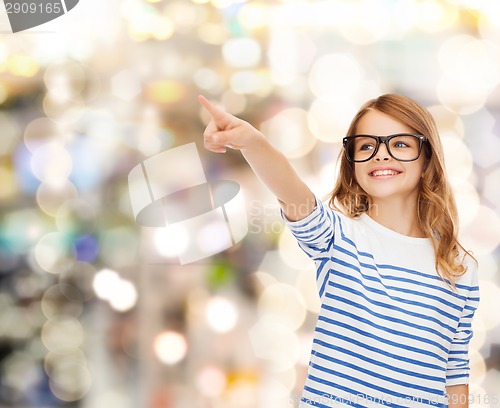 Image of cute little girl in eyeglasses pointing in the air