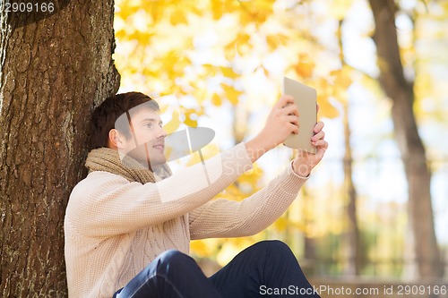 Image of smiling young man with tablet pc in autumn park