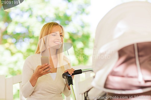 Image of happy mother with smartphone and stroller in park