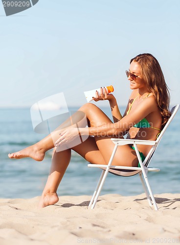 Image of smiling young woman sunbathing in lounge on beach