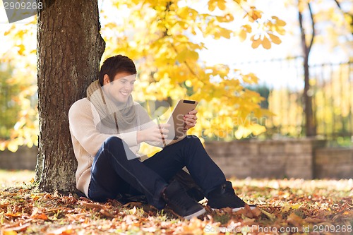 Image of smiling young man with tablet pc in autumn park